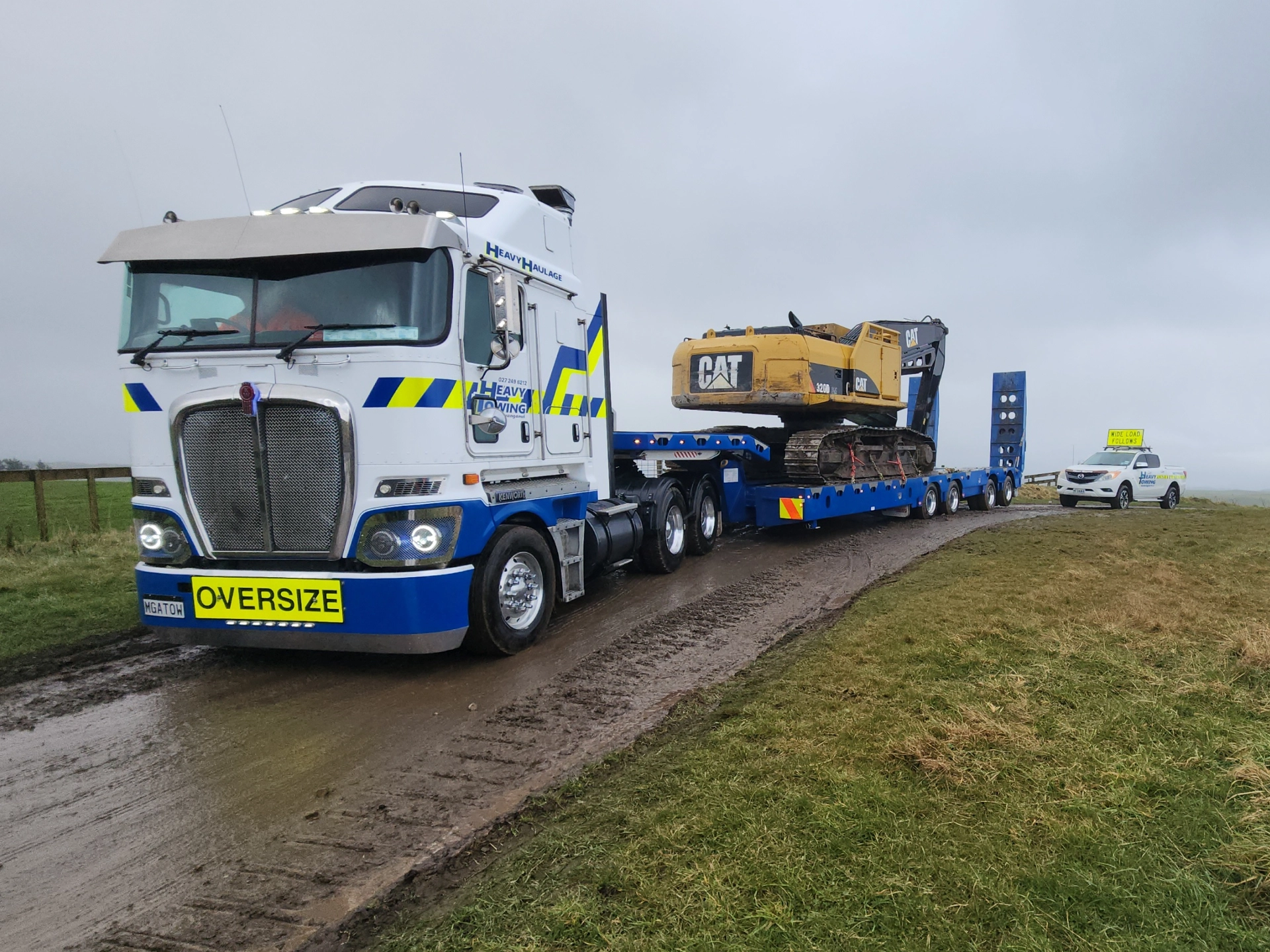 Heavy Towing Kenworth with an OVERSIZE sign carrying a CAT excavator, escorted by a pilot vehicle
