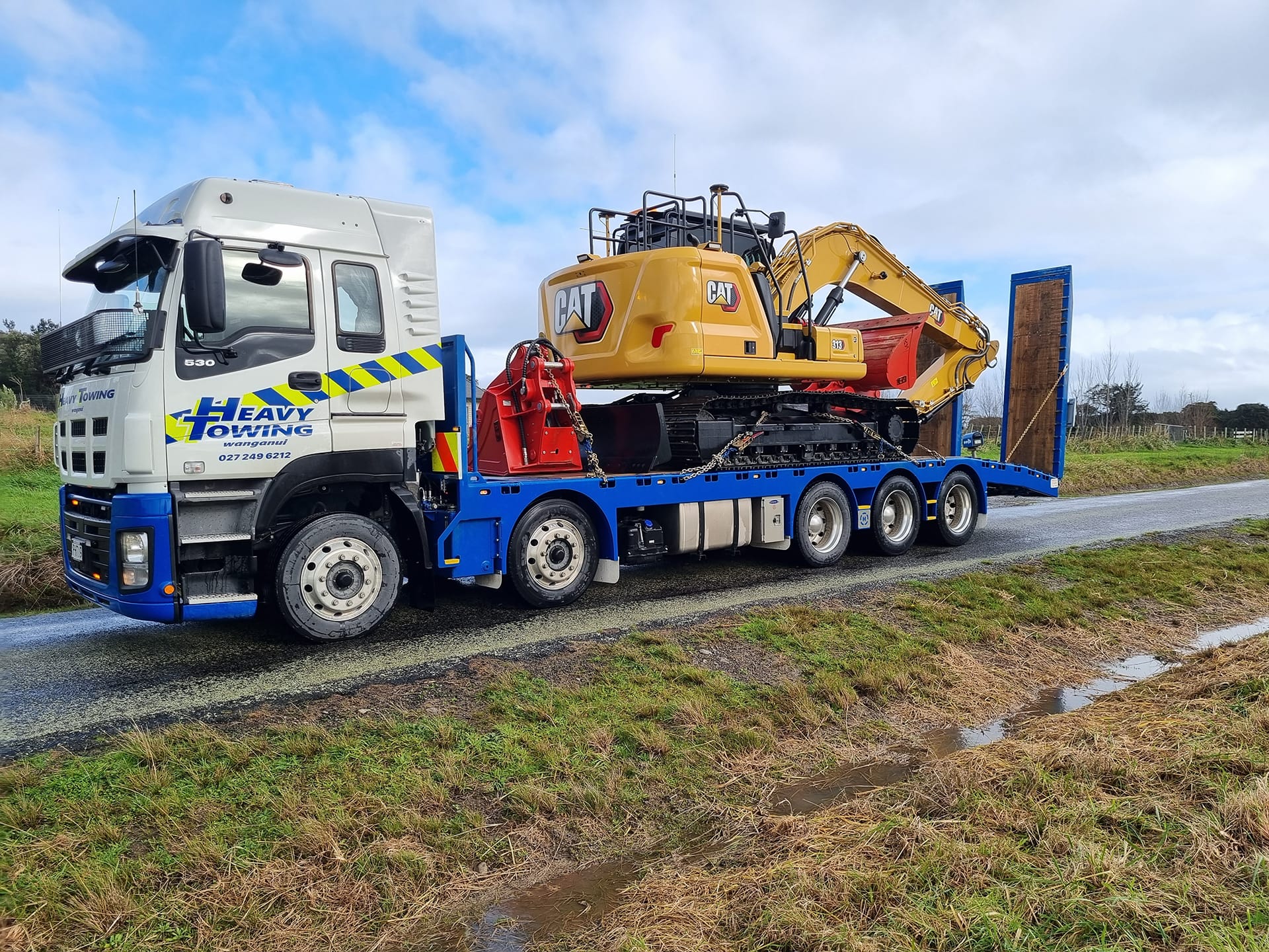 Heavy Towing truck carrying a CAT excavator on a low-loader along a rural road